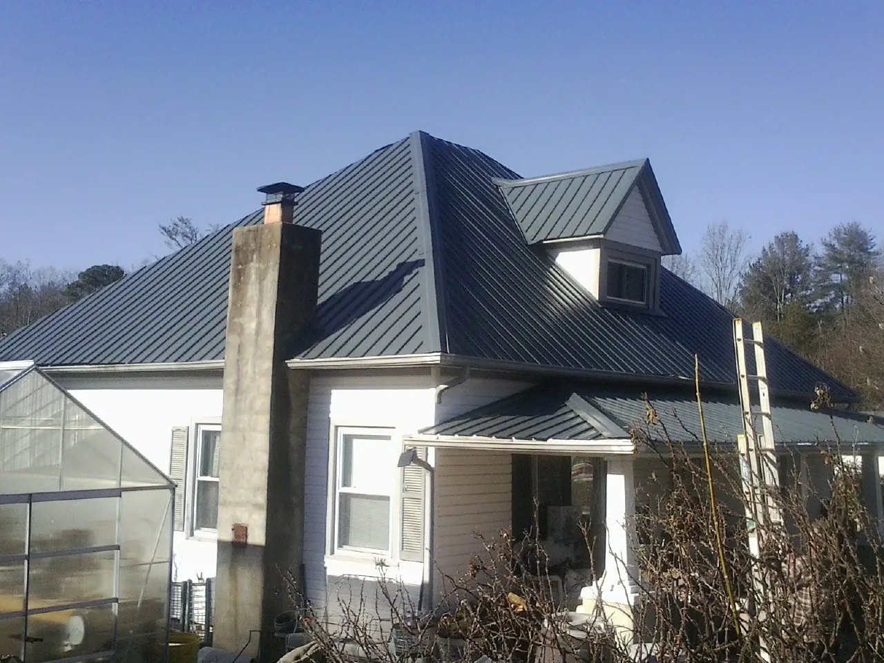 Dark blue standing seam metal roof on a white farmhouse with dormer — Slate & Tile Roof Repair by Roofing Brothers in Donald