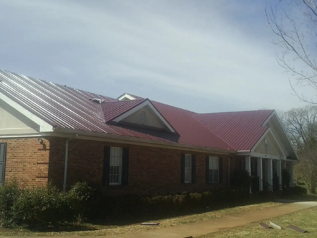 Red metal roof with gabled entries on a long brick building, from a Hail Damage Roof Repair job in Donald