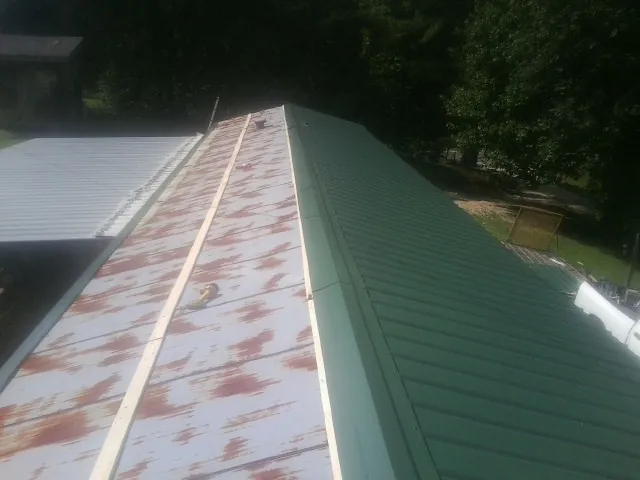 Old rusted panels beside newly installed green metal roofing — Wind Damage Roof Repair by Roofing Brothers in Donald