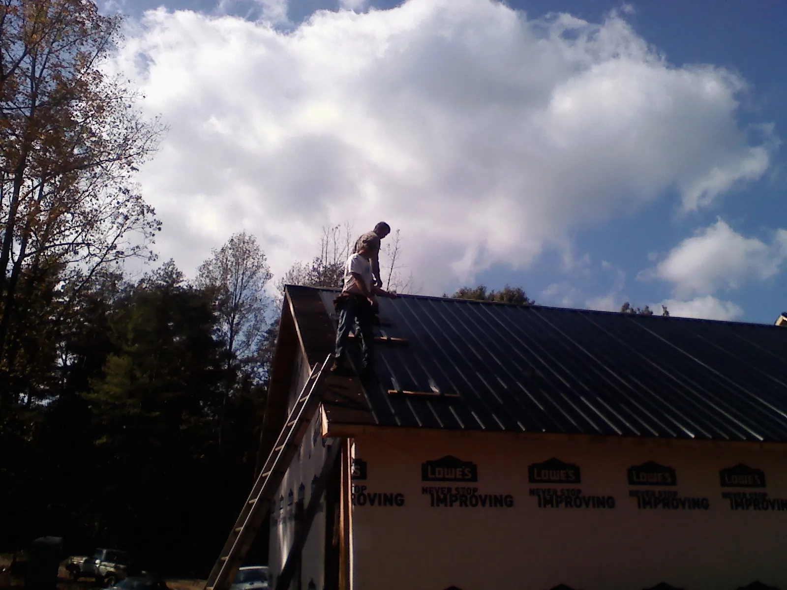 Roofer fastening dark metal panels high against a cloudy sky, from a Roof Inspection job in Donald