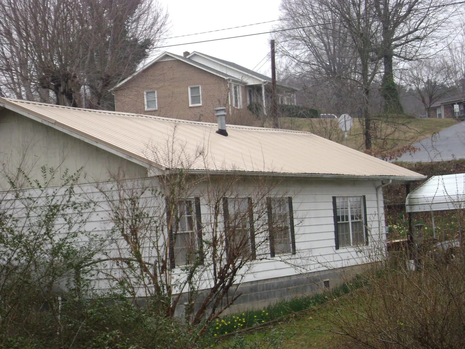 Tan metal roof on a white sided house set into a hillside — Commercial Roofing by Roofing Brothers in Donald