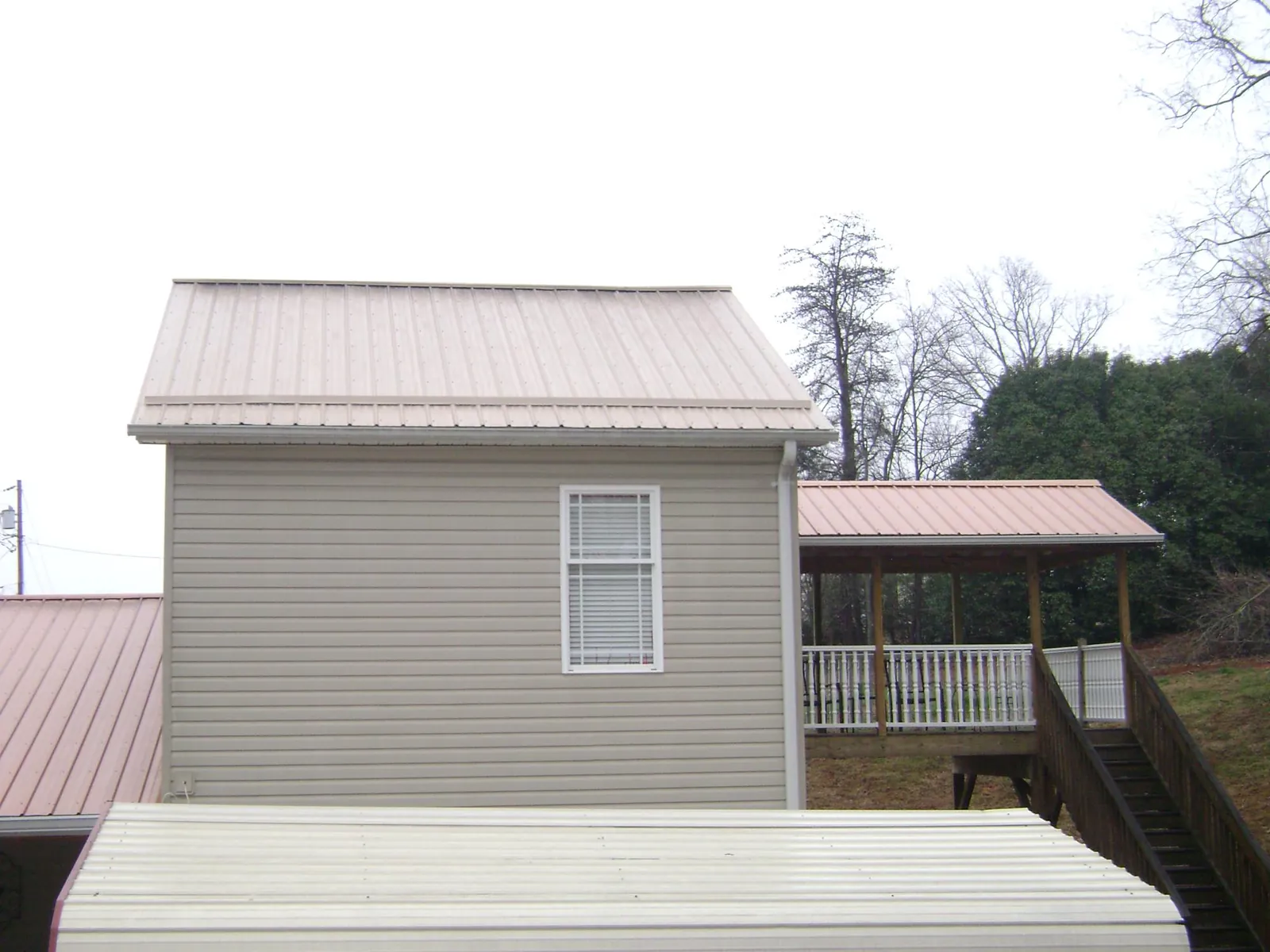 Tan metal roofs on a two story addition and attached porch, from a Roof Replacement job in Donald